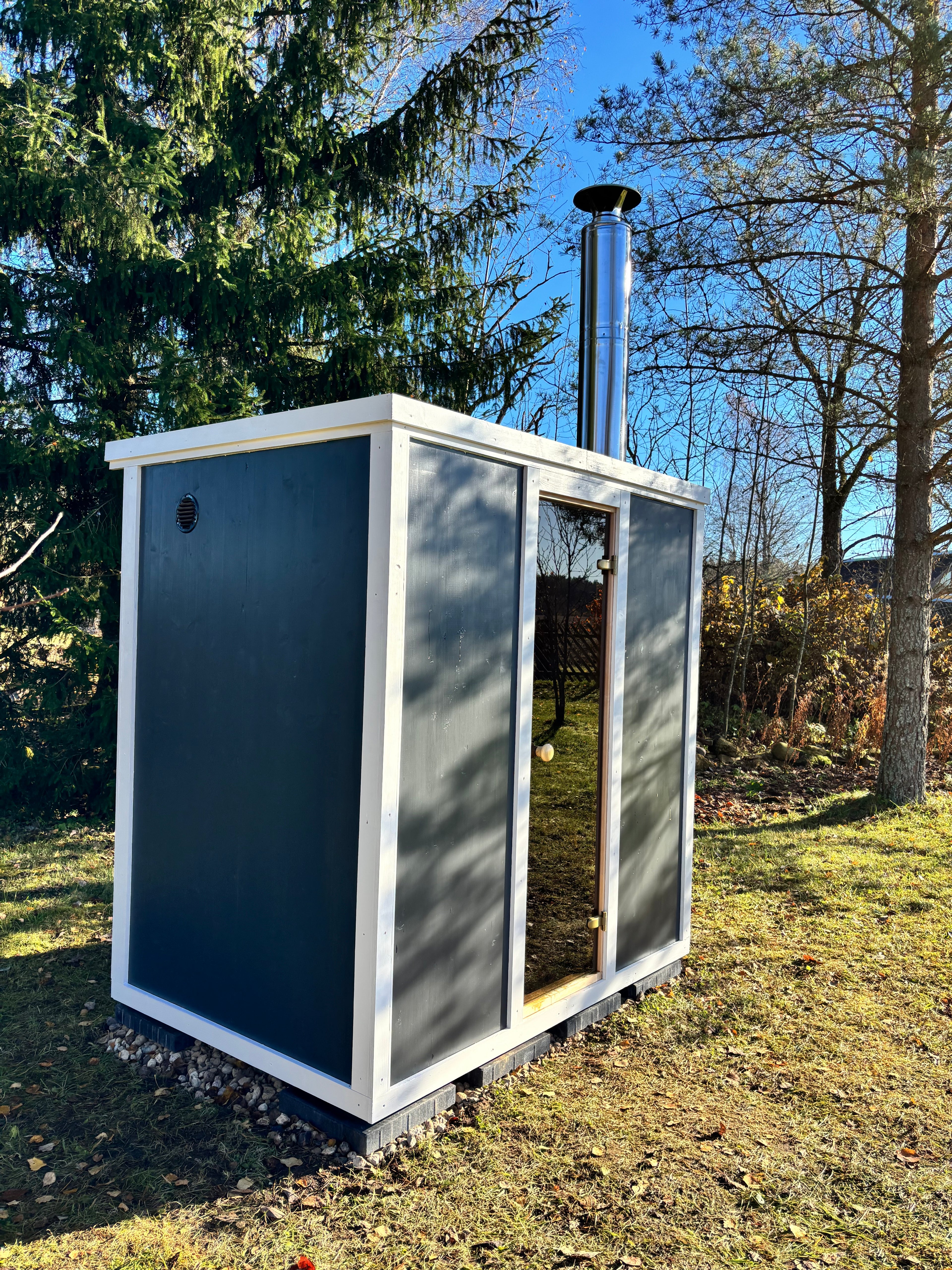 Tumma CLT-rakenteinen pihasauna syksyisessä pihapiirissä - moderni ja kompakti ulkosauna puukiukaalla