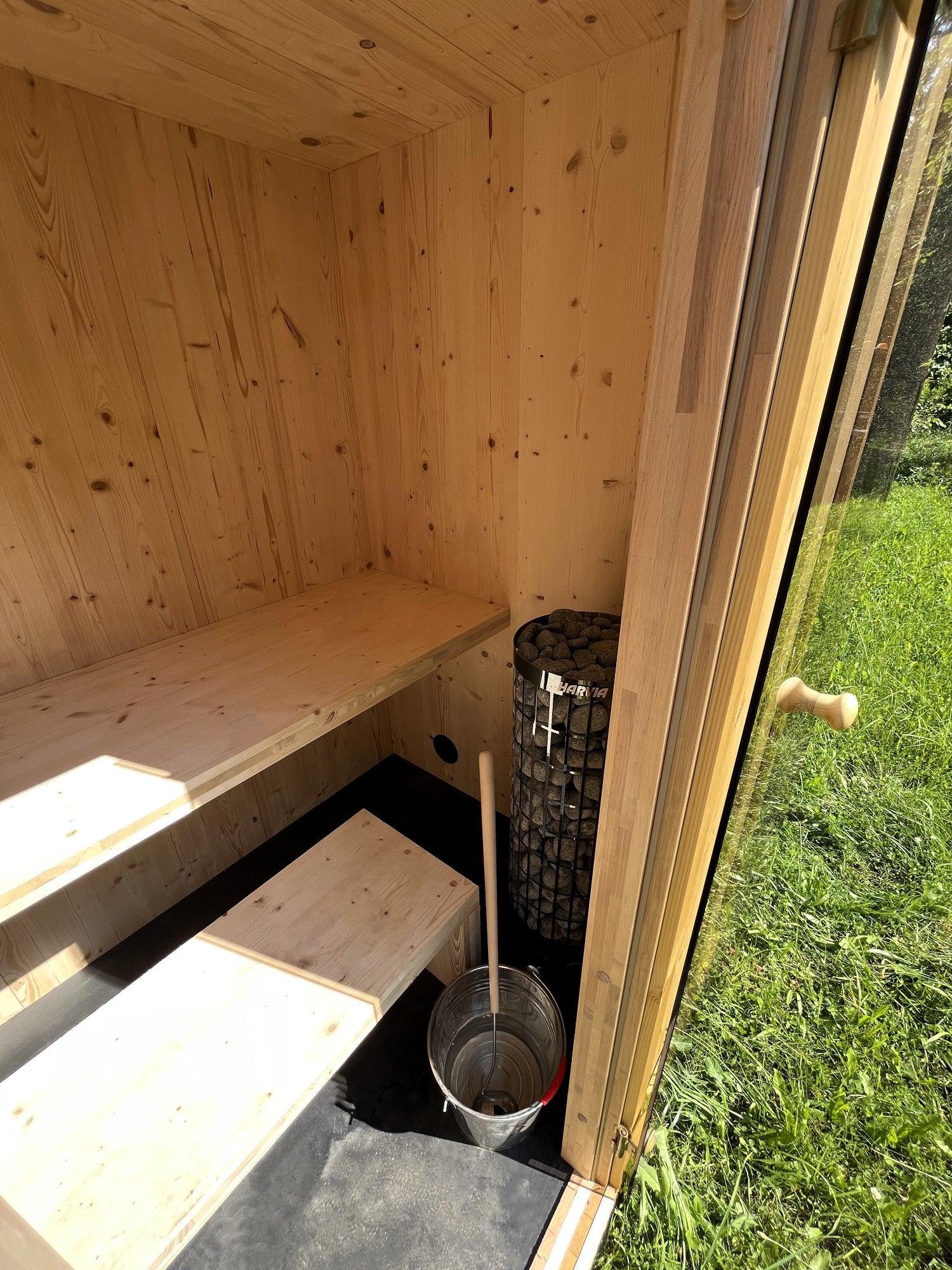 CLT-valmisteisen pihasaunan sisätilat - harvian kiuas, vaalea puupinta ja lauteet